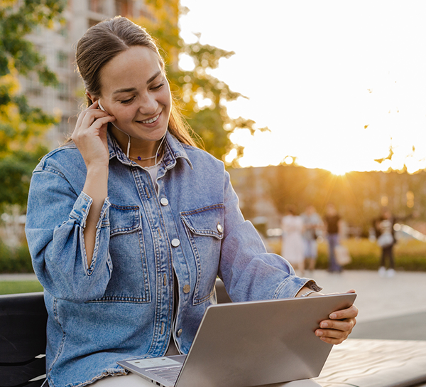 Woman sitting outside with laptop and headphones and smiling