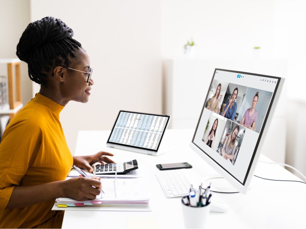 Woman is sitting at a desk in front of a computer and is in a video conference.