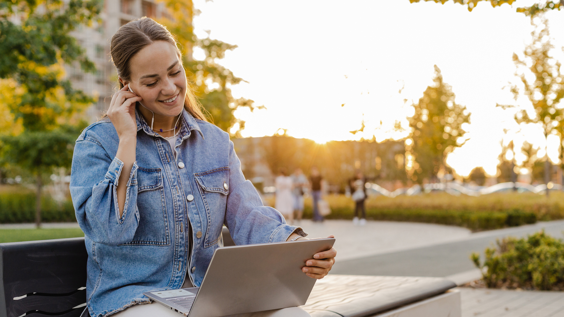 Student sits outside with laptop and headset and smiles